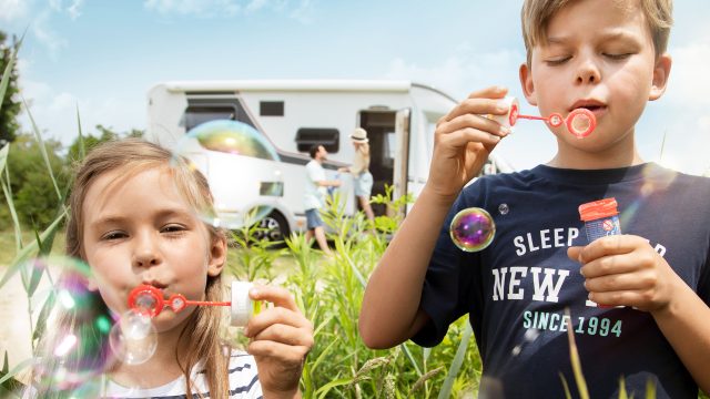 To barn som blåser såpebobler i forgrunn av en bobil.